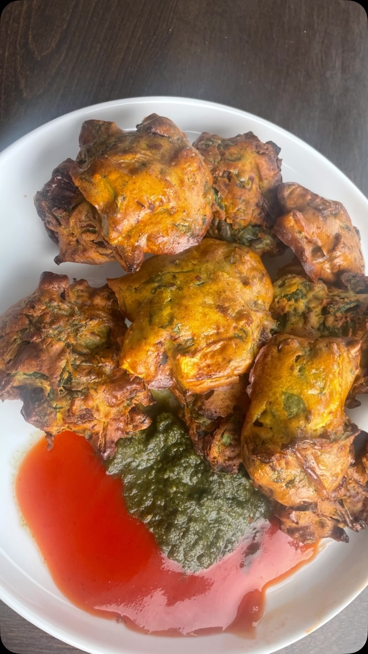 #airfrier #pakora #Few foods carry the kind of soul-warming nostalgia that pakoras do. Across India, these crispy, spiced fritters have graced street food carts, family kitchens, and roadside dhabas for generations. Pakoras are synonymous with the monsoon season — the kind of snack you reach for when rain is hammering the windows and a cup of chai is already brewing on the stove.

This air fryer version is a game-changer. You get the same deeply spiced, shattering crunch on the outside and a soft, steamy interior — without the liters of oil, the splatter, or the lingering smell -  ready in under 30 minutes! No frying. Eat guilt free and enjoy any time. Simple and tasty.

Ingredients 
2 cups palak (spinach) - washed, dried and finely chopped
1 small onion - finely chipped
2  green chilies - finely chopped (adjust as per taste)
1 cup besan (gram flour)
1 tbsp rice flour/ corn flour ( optional, for extra crisp)
1 tsp ajwain (carom seeds)
1 tsp red chili powder (adjust as per taste)
½ tsp turmeric powder 
1 tsp garam masala 
Salt to taste
Oil for brushing or spray

Method

In a bowl, add besan, palak, onion, rice flour, green chilies and spices
Mix well and let it rest for a few minutes since spinach and onions will release water. Add extra water (little at a time) to make a thick batter( pakora - style). Mix very well. 
Keep aside  for 15 minutes. 
Preheat air fryer @ 190 C or 375 F 
Lightly grease the air fryer or put on parchment paper. Mix pakora mix, shape pakora with a spoon or hand and put in an air fryer. Keep space in between and do not over crowd.
Bake for 5-7 minutes,  then apply oil on top with a brush or spray. 
Bake for 5-7 minutes or until golden brown.
Flip pakoras, apply oil on reverse side and bake for another 5-7 minutes
Serve with green chutney, imli chutney and masala chai