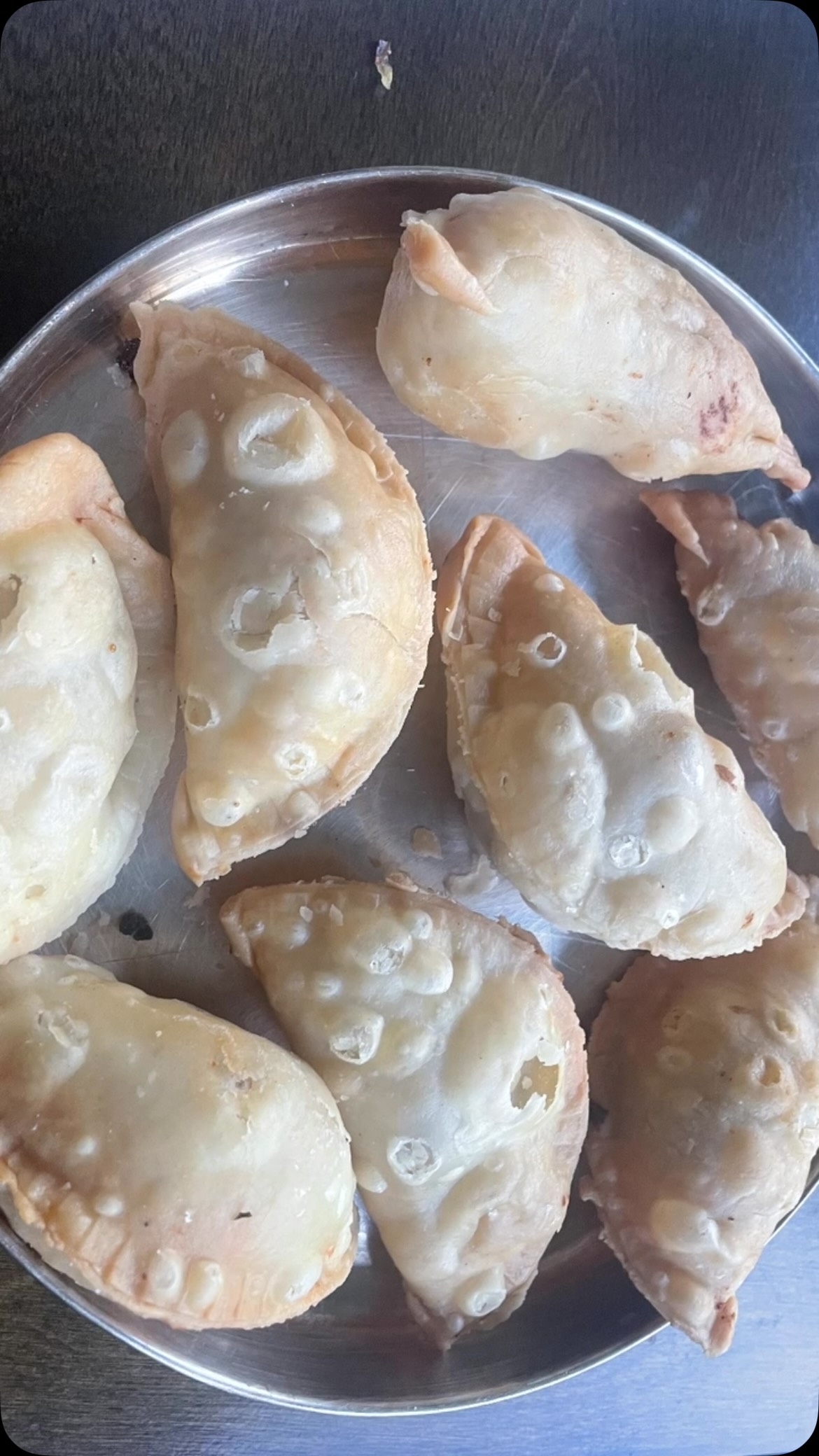 #mawagujiya😋❣️#With Any festivals coming around, now is a great time to make sweets! One of my favorite #recipeon👇🏾 desserts is mawa gujiya. Gujiya is a delicious Indian sweet with a crispy outer crust, stuffed with a sweet filling. It’s made with flour, sugar, ghee, nuts, and most importantly mawa. It can also have stuffed sooji but the mawa taste is better to me. It takes a little patience, but it’s definitely worth it!
Ingredients 
Serves 20
2 ½ cups all purpose flour
1 tbsp semolina (suji)
Pinch of salt 
3 tbsp ghee
Oil for frying 

For the filling 
1 cup mawa, roasted 
½ cup sugar 
1 tbsp coconut powder (nariyal ka burada)
1 tbsp cardamom powder
8 to 10 almonds - finely cut
8 to 10 cashew nuts - finely cut
20 raisins
For syrup 
¼ cup water
1 cup sugar
10 threads saffron (kesar)

For garnish 
15 pistachios
1 piece silver foil (chandi varak) - optional 
Gujiya maker 
Take a wide bowl and mix flour, suji and ghee for a minute or until crumbly. Take the flour in your palm and try to make a small ball - if you can’t, add more ghee.
Now add water slowly and make a medium soft dough, then spread oil on the dough surface. Cover the dough with soaked fabric and let it rest for about 30 minutes.
Take another bowl, and add mawa, coconut powder, cardamom powder, almond, cashew nuts, raisins and sugar. Mix everything, keep aside.
Take the dough and make 20 pieces of uniform size.
Take one piece and roll it out, about 4 to 5 inches. Add about 1 tbsp of the mawa mixture.
Take a little water and apply on the edges using your finger. Then press in the gujiya maker (or press it closed into a ½ moon shape yourself), press lightly, and keep aside. 
Do all the same manner. Make sure to seal the gujiya well, otherwise when frying, the gujiya filling will fall out.
To make the syrup, take a wide pan and add water and sugar, on medium heat. Cook for about 5 minutes or until threads form when mixing. Turn off the heat.
Take a fry pan with oil and start on slow heat. Wait until the oil is hot.
Then, add the gujiyas, making sure it is not crowded. Fry both sides until golden brown. Fry all in the same manner, then keep on a paper towel.
Take the sugar syrup and remove #garnish .